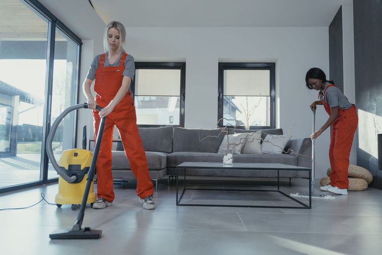 Reinigungskräfte in Arbeitskleidung reinigen einen hellen Wohnraum.